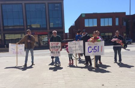 Rally participants listening to speakers at the anti-Bill C-51 rally in downtonw Sudbury today, including Christine Lortie (holding the baby) and Marxist-Leninist Party representative David Starbuck (holding the "Stop Harper" sign). (Photo by Scott Neigh)